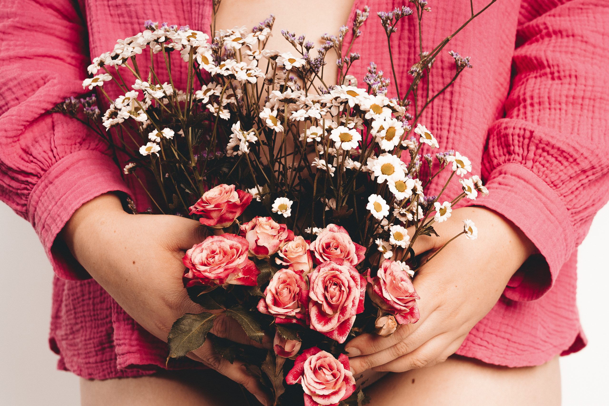 Frau in magentafarbenem Hemd hält Blumen vor ihrem Bauch und Intimsphäre