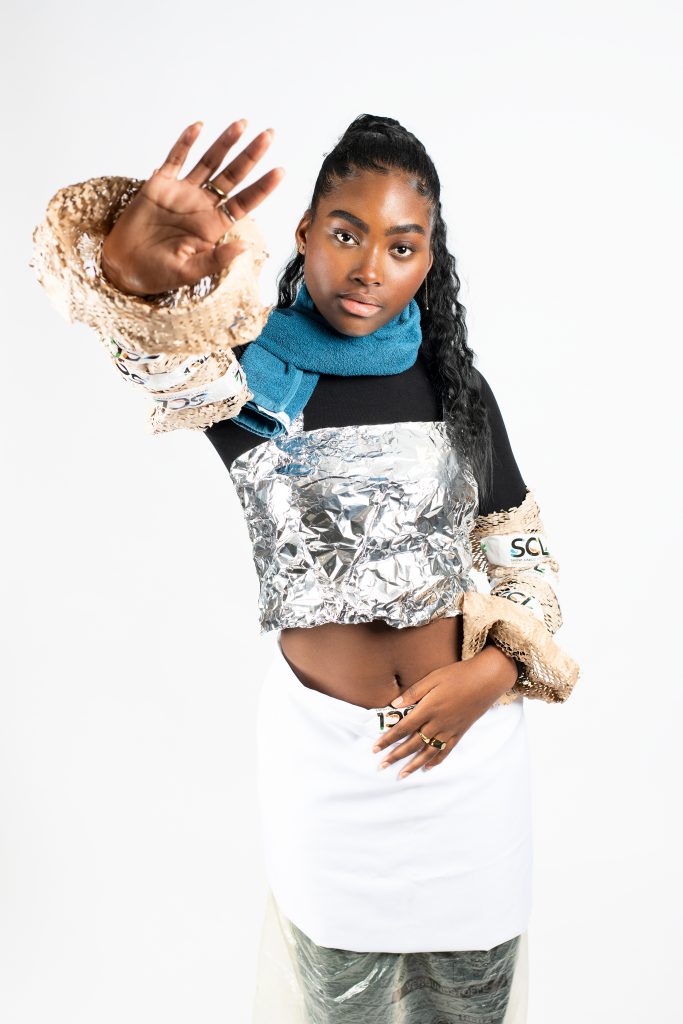 Modefotografie: Junge Frau, die recycelte Materialen als Mode verwendet, wie Alufolie als Oberteil und ein Handtuch als Schaal